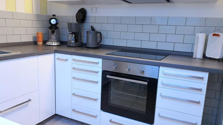 Eine moderne Küche mit weißen Schränken und grauen Arbeitsflächen. Auf der Arbeitsplatte stehen verschiedene Küchengeräte wie ein Wasserkocher und eine Kaffeemaschine.