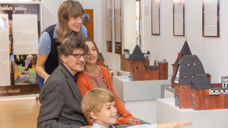 Eine Familie betrachtet Miniaturmodelle von Schlössern in einem Museum. Die Kinder zeigen begeistert auf ein Modell.