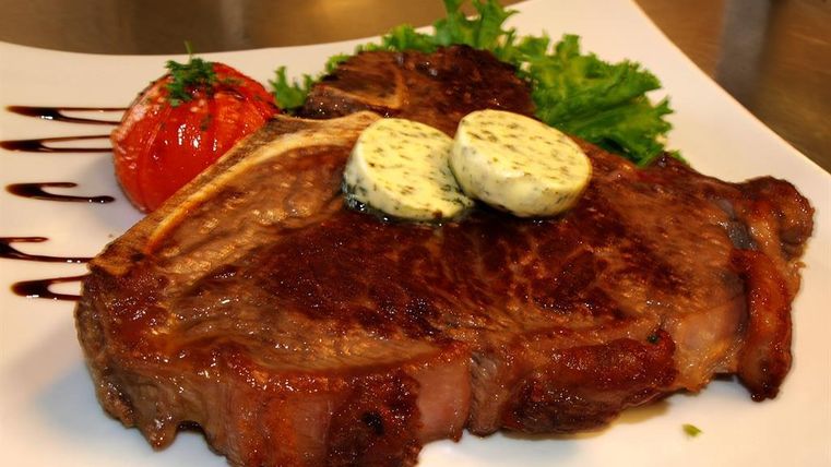 Ein saftiges Steak mit Kräuterbutter, serviert mit einem gebratenen Tomaten und frischem Salat. Der Teller ist elegant angerichtet und wirkt appetitlich.