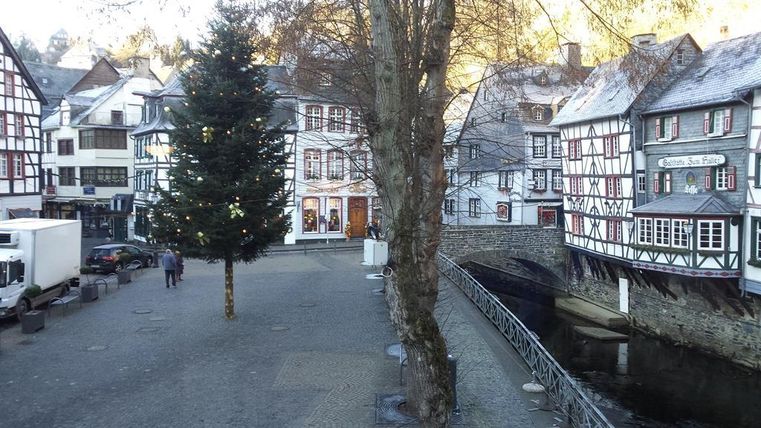 Eine malerische Stadt mit Fachwerkhäusern und einem kleinen Wasserlauf. In der Mitte steht ein Weihnachtsbaum, der festlich geschmückt ist.