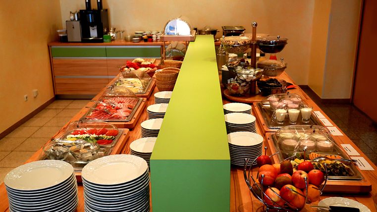 Ein reichhaltiges Frühstücksbuffet mit frischem Obst, Brot und verschiedenen Speisen. Die Tische sind ordentlich gedeckt und laden zum Schlemmen ein.