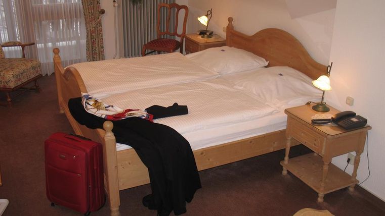 Ein gemütliches Hotelzimmer mit zwei Betten und einem roten Koffer. Es gibt einen Tisch, einen Stuhl und eine Lampe, die eine einladende Atmosphäre schaffen.