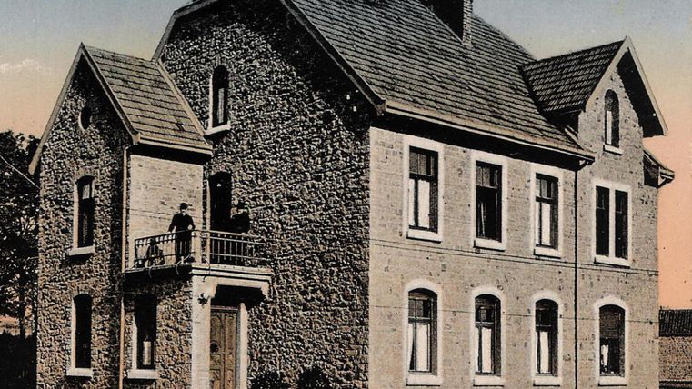 Ein historisches Pfarrhaus aus Stein mit einem Balkon. Die Fassade zeigt mehrere Fenster und ein Dach aus Ziegeln.