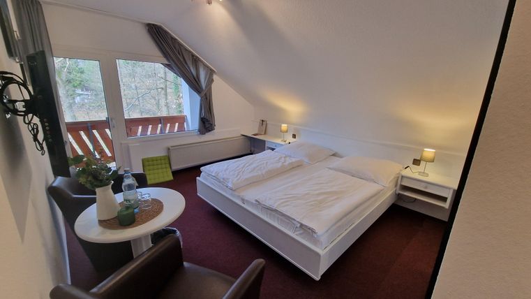 Ein gemütliches Zimmer mit einem Doppelbett und zwei Sesseln. Große Fenster sorgen für viel Licht und einen Blick nach draußen.
