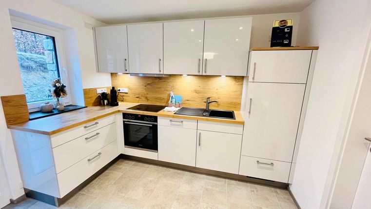 Eine moderne Küche mit weißen Möbeln und Holzdetails. Sie verfügt über eine Spüle, einen Herd und einen Kühlschrank.