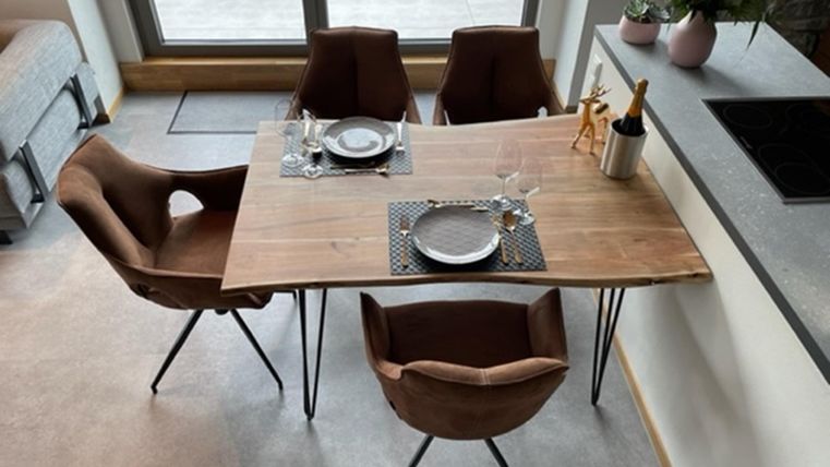 Ein modern gestalteter Esstisch aus Holz mit vier Stühlen. Auf dem Tisch sind Teller, Gläser und eine dekorative Blumenvase mit frischen Blumen.