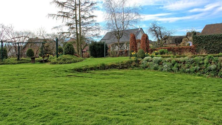 Ein gepflegter Garten mit grünem Rasen und bunten Blumen. Im Hintergrund sind einige Häuser und Bäume zu sehen.
