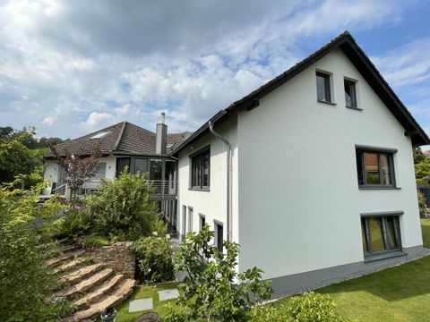 Ein modernes Haus mit weißen Wänden und einem hellen Dach. Der Garten ist grün und gepflegt mit einer Treppe aus Steinen.