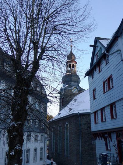 Eine schmale Gasse mit historischen Gebäuden und einem Kirchturm im Hintergrund. Die Szenerie ist winterlich und ruhige Atmosphäre.