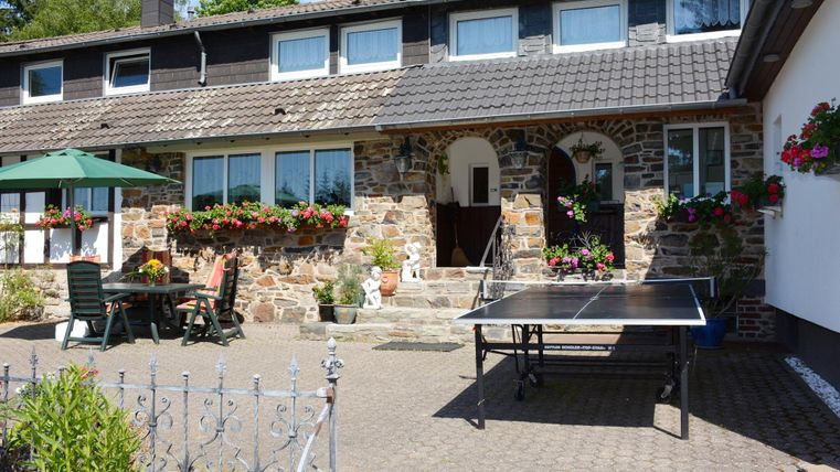 Ein gemütliches Haus mit einem schönen Innenhof und Blumenblühten. Im Vordergrund steht ein Tischtennistisch unter einem Sonnenschirm.