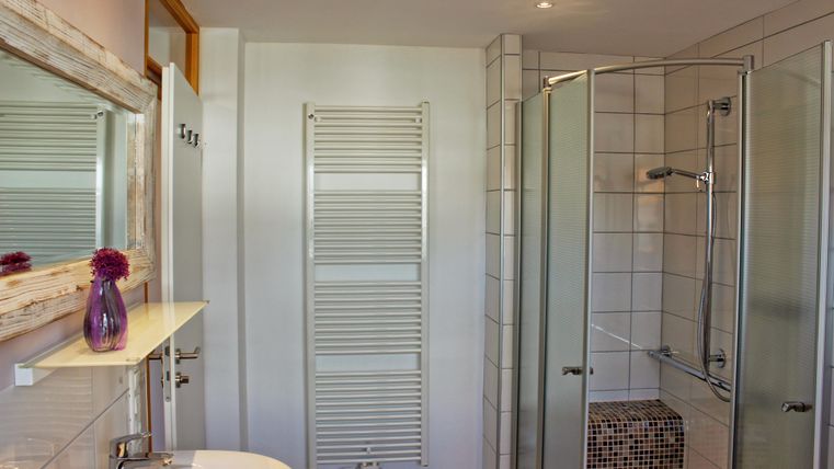 Ein modernes Badezimmer mit einer Dusche und einem Waschbecken. Die Wände sind hell gefliest, und ein Handtuchhalter sowie ein großer Spiegel sind sichtbar.