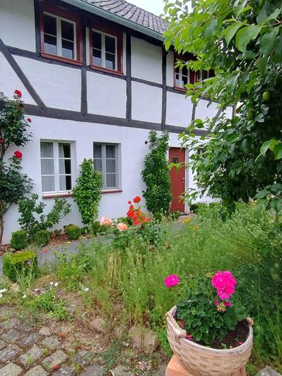 Ein traditionelles Fachwerkhaus mit einem gepflegten Garten. Bunte Blumen und grüne Pflanzen schmücken den Eingang.
