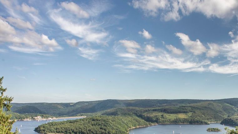 Eine schöne Landschaft mit einem ruhigen Gewässer und sanften Hügeln. Der Himmel ist klar mit einigen Wolken.