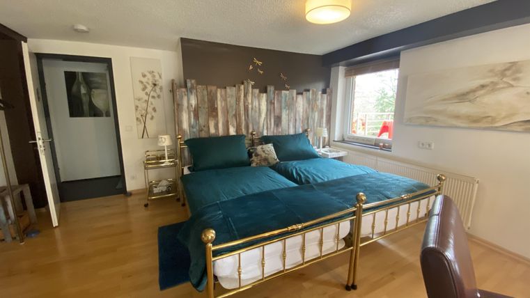 Ein gemütliches Schlafzimmer mit zwei Einzelbetten und einem goldenen Bettrahmen. Der Raum hat einen warmen Holzfußboden und Fenster mit Blick ins Freie.