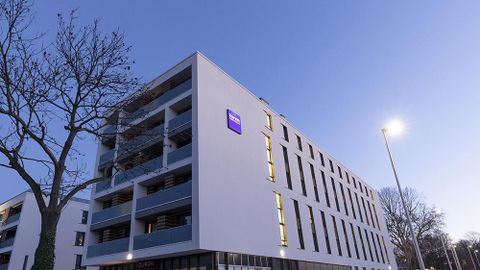 Ein modernes Gebäude mit einem klaren, weißen Design. Es ist Abend und der Himmel ist leicht dunkelblau.