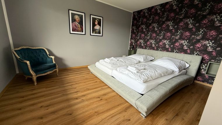Ein modernes Schlafzimmer mit einem großen Bett und zwei Kissen. An der Wand hängen zwei Bilder, und in der Ecke steht ein eleganter Sessel.