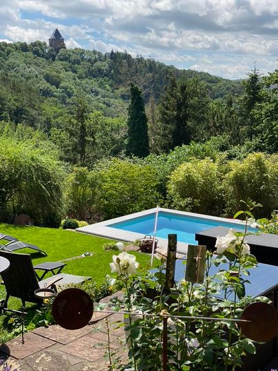 Ein schöner Garten mit einem Pool und grünen Pflanzen. Im Hintergrund sind Hügel und ein Aussichtsturm zu sehen.
