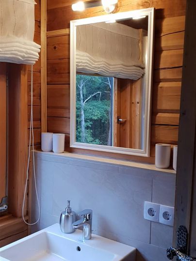 Ein modernes Badezimmer mit einem weißen Waschbecken und einem großen Spiegel. Die Wände sind aus Holz und es gibt ein Fenster, das Licht hereinlässt.