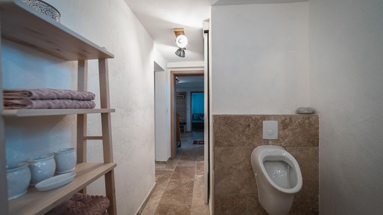 Ein sauberer, heller Flur mit einem Urinal und einem offenen Durchgang. Regale mit Handtüchern und Schalen ergänzen den Raum.