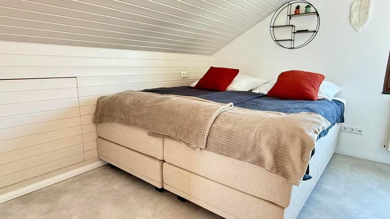 Ein gemütliches Schlafzimmer mit einem Doppelbett und roten Kissen. An der Wand hängen dekorative Elemente und das Licht ist hell.