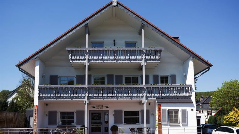 Ein charmantes Hotelgebäude im Alpenstil mit zwei Balkonen. Die Fassade ist weiß, und der Himmel ist klar und blau.