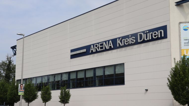 Ein modernes Gebäude mit der Aufschrift "ARENA Kreis Düren". Es ist gut beleuchtet und hat große Fenster.
