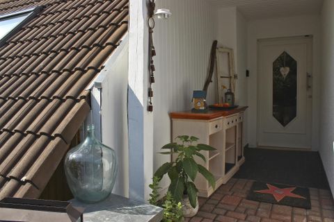 Ein einladender Eingangsbereich mit einer hellen Tür und einem Holztisch. Daneben stehen Pflanzen und ein großes Glasgefäß.
