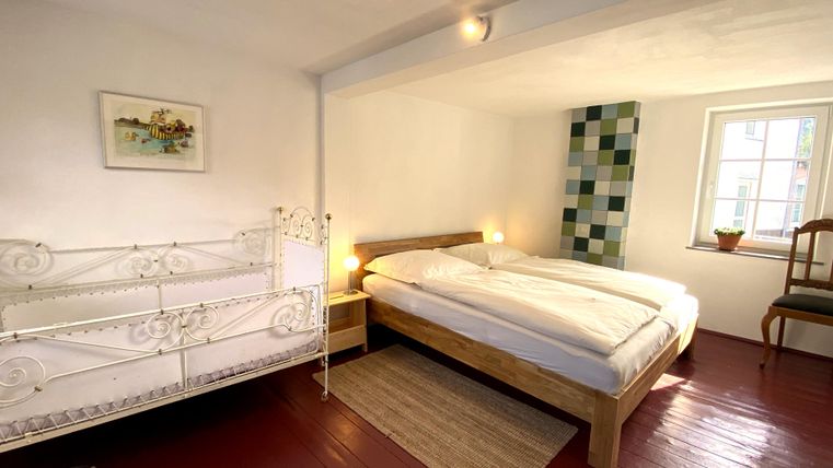 Ein gemütliches Schlafzimmer mit einem Doppelbett und einem Kinderbett. Der Raum hat helle Wände und einen Holzfußboden.
