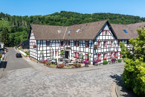 Ein charmantes Fachwerkhaus an einer ruhigen Straße. Es ist von grünen Bäumen umgeben und blühenden Pflanzen geschmückt.