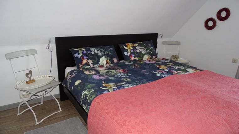 Ein gemütliches Schlafzimmer mit einem großen Bett und floralen Kissen. Neben dem Bett steht ein kleiner Tisch und eine schöne Dekoration an der Wand.