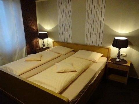 Ein gemütliches Schlafzimmer mit einem Doppelbett und zwei Nachttischen. Die Wände sind in sanften Farben gehalten, und sanftes Licht spielt eine einladende Atmosphäre.