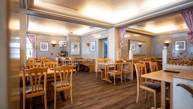 Ein gemütliches Restaurant mit Holzstühlen und Tischen. Die Wände sind mit dekorativen Bildern und Vorhängen geschmückt.