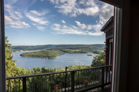 Eine beeindruckende Aussicht auf einen ruhigen See umgeben von grünen Hügeln. Die Mischung aus Himmel und Wolken schafft eine entspannte Atmosphäre.
