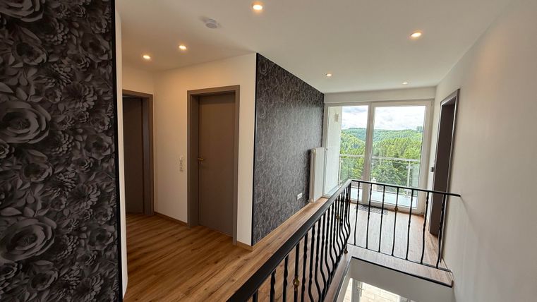 Ein moderner Flur mit Holzfußboden und eleganten Wänden. Große Fenster bieten einen Blick auf die grüne Umgebung.