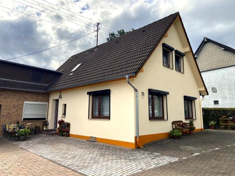 Ein modernes Haus mit einem schrägen Dach und mehreren Fenstern. Der Eingang ist gepflastert und mit Pflanzen dekoriert.