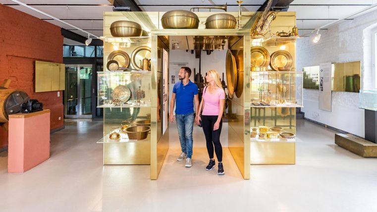 Ein modernes Museum mit glänzenden Vitrinen, die verschiedene Objekte zeigen. Zwei Personen erkunden interessiert die Ausstellungen.