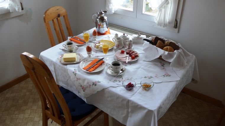 Ein liebevoll gedeckter Frühstückstisch mit verschiedenen Leckereien. Darauf befinden sich Brötchen, Marmelade, Obst und Getränke.