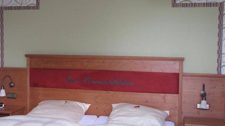 Ein gemütliches Schlafzimmer mit einem Holzbett und weißen Bettdecken. Die Wände sind mit einem grafischen Muster und einer grünen Akzentfläche dekoriert.
