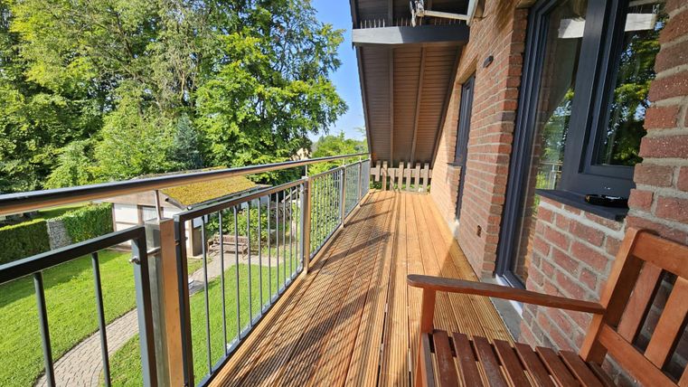 Ein sonniger Balkon mit Holzbohlen und einer schönen Aussicht auf den Garten. Die Umgebung ist grün und einladend.