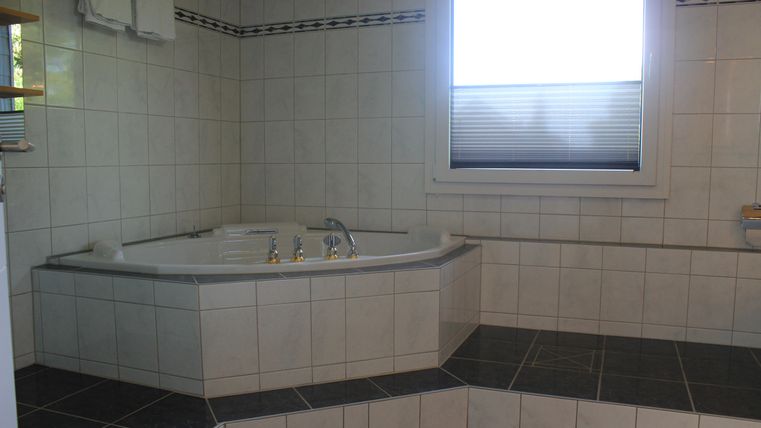Ein modernes Badezimmer mit einem großzügigen Whirlpool und hellen Fliesen. Ein Fenster sorgt für natürliches Licht und eine angenehme Atmosphäre.