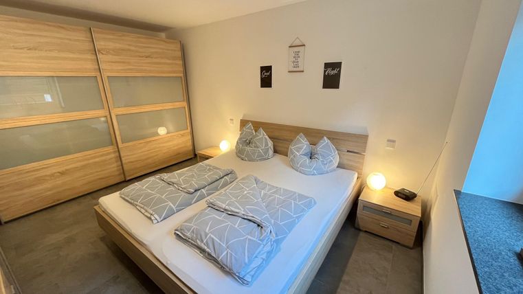 Ein modernes Schlafzimmer mit einem Doppelbett und zwei Kissen. Die Möbel sind aus hellem Holz und es gibt sanfte Beleuchtung.