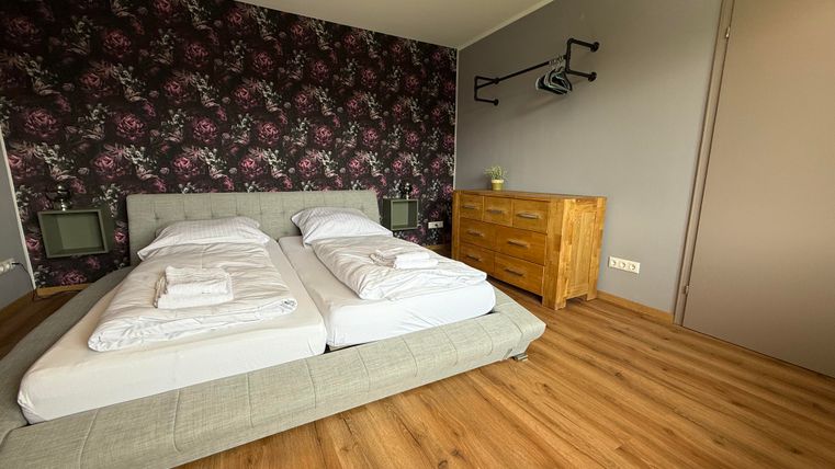 Ein modernes Schlafzimmer mit einem bequemen Doppelbett und einem Holzschrank. Die Wände sind mit einem floralen Muster dekoriert, und der Boden ist aus Holz.