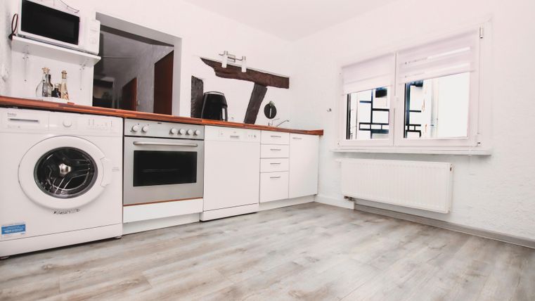 Eine moderne Küche mit einem Waschmaschine, Ofen und weißem Schrank. Der Boden ist aus hellem Holz und es gibt ein großes Fenster.
