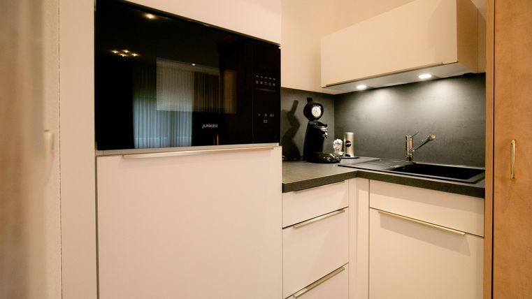 Eine moderne Küche mit weißen Schränken und einem schwarzen Arbeitsbereich. Es gibt einen Kühlschrank, eine Kaffeemaschine und eine Spüle.