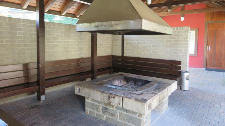 Ein Grillplatz unter einem überdachten Bereich mit Holzbänken. Der Grill ist aus Stein und hat einen großen, schrägen Abluftschacht.