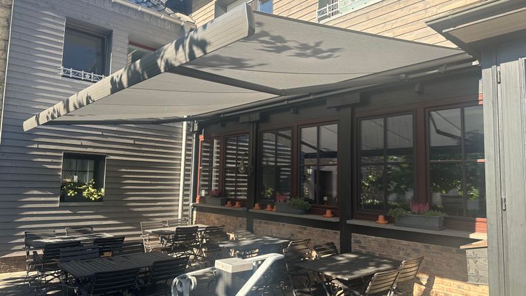 Eine Terrasse mit einem großen Markise und mehreren Tischen. Das Restaurant ist von einem schönen Gebäude umgeben.