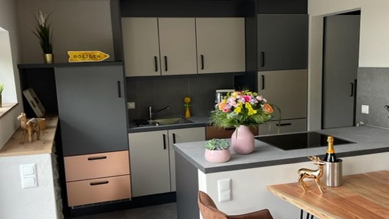 Eine moderne Küche mit grauen und hellen Schränken. Auf dem Tisch steht eine Vase mit bunten Blumen.