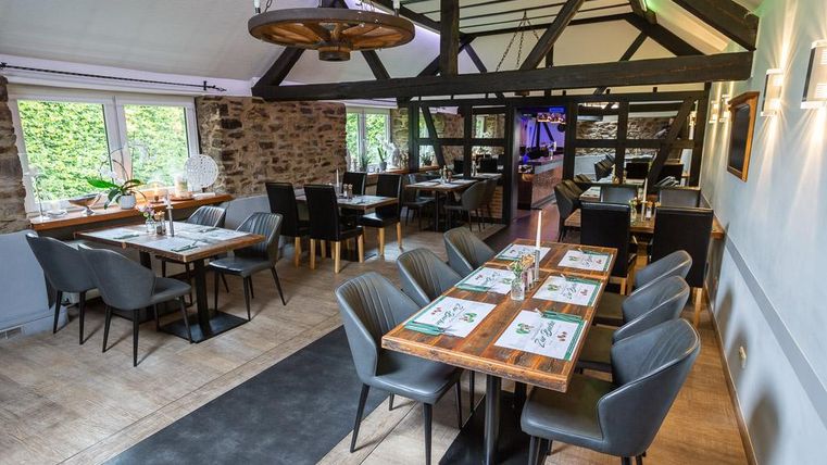 Ein modernes Restaurant mit Holzbalken und eleganten Tischen. Die Einrichtung ist hell und einladend, mit großen Fenstern, die viel Licht hereinlassen.