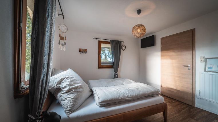 Ein gemütliches Schlafzimmer mit einem Doppelbett und einem großen Fenster. Die Wände sind hell, und es gibt dekorative Elemente wie einen Traumfänger.
