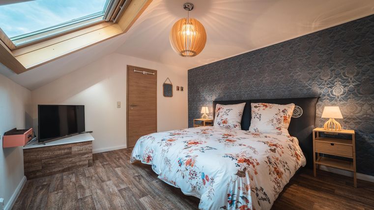 Ein modernes Schlafzimmer mit einem großen Bett und einer blumigen Bettdecke. Der Raum verfügt über einen Fernseher, Nachttische und ein Dachfenster.